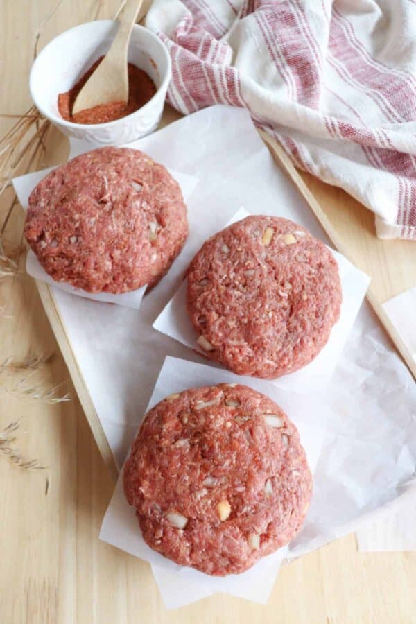 Raw hamburger patties stacked between sheets of parchment paper ready to be frozen.