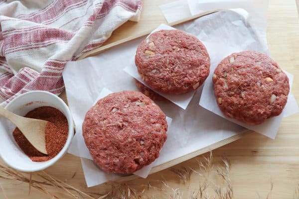 Three raw hamburger patties on parchment paper.