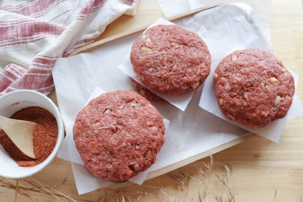 How to Bake Hamburger Patties Process with raw patties stacked on parchment paper.