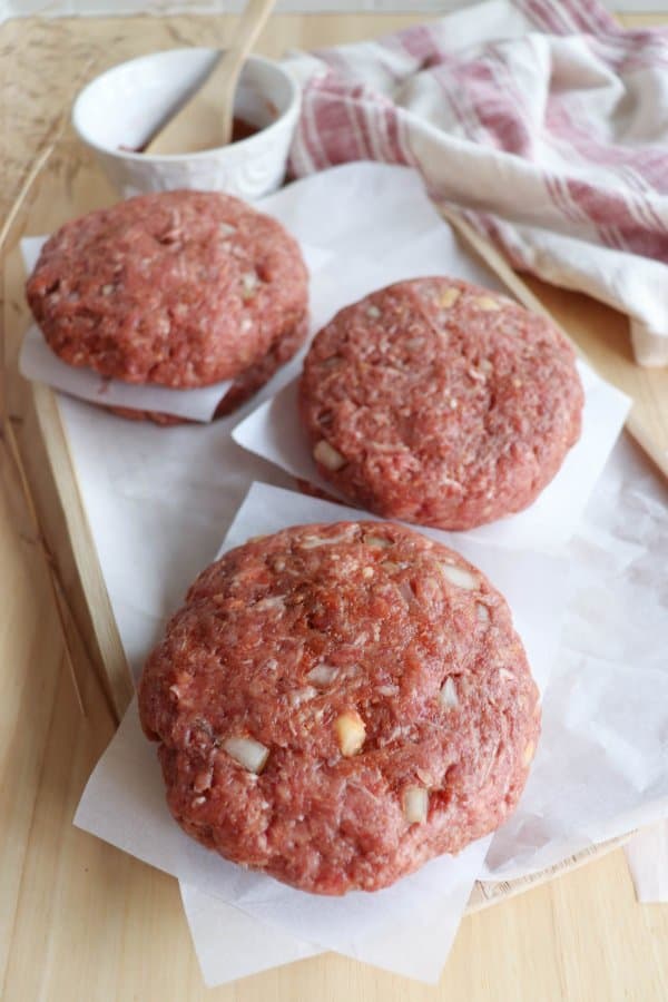 Raw hamburger patties stacked between sheets of parchment paper ready to freeze.