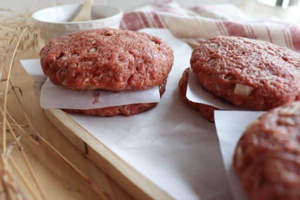 Close up of raw hamburger patties stacked between sheets of parchment paper.