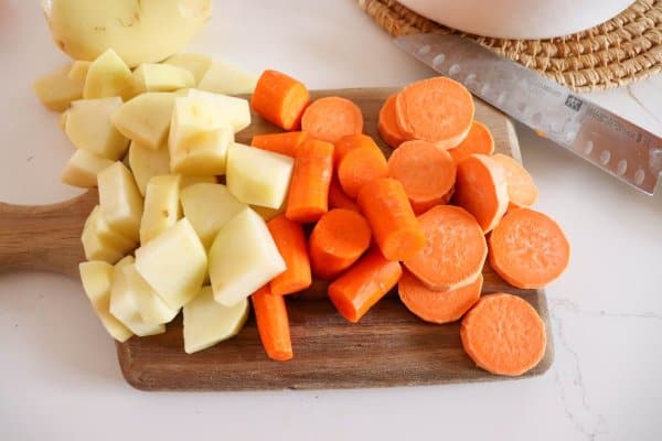 Potatoes, carrots and Yams cut into chunks on a wooden cutting board.