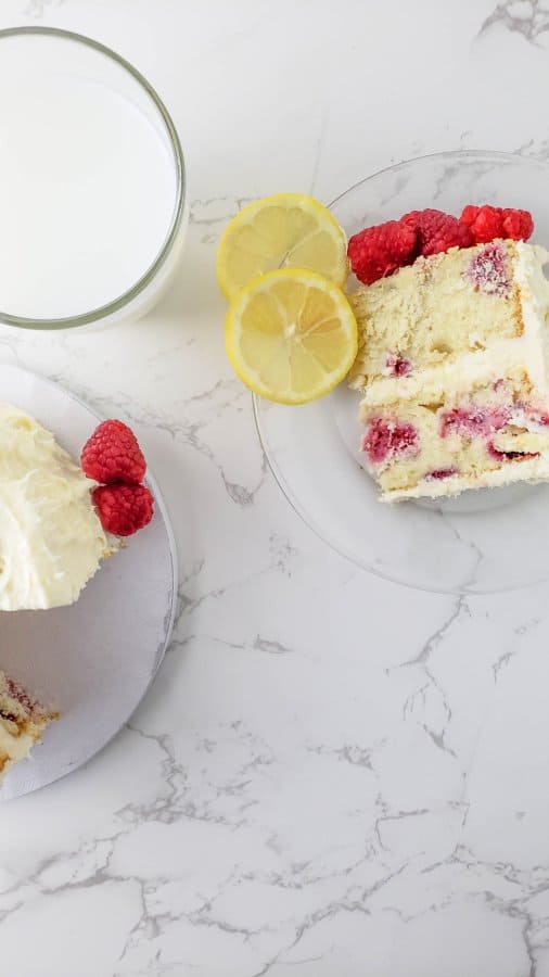 A slice of the raspberry cake recipe on a plate with 2 slices of lemon and some fresh raspberries.
