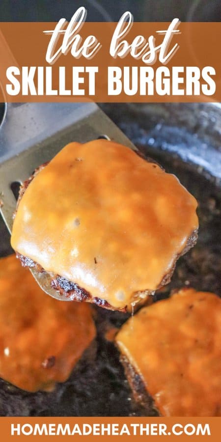 Cooked burger topped with melted orange cheese on a metal spatula with a cast iron skillet in the background.