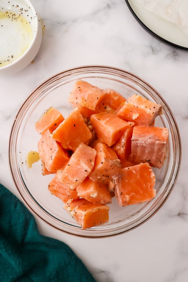 Salmon cubes in a glass bowl with seasonings.