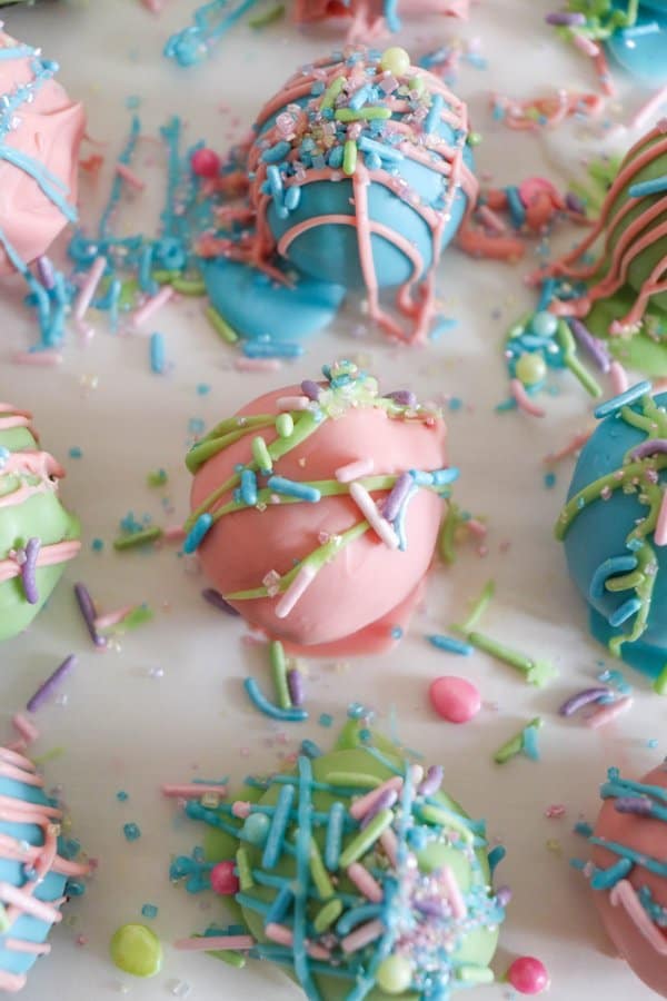 Oreo cake balls covered in pink, blue and green chocolate with colorful drizzle and sprinkles.