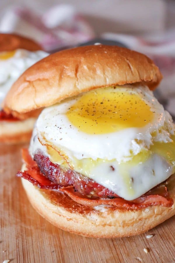 Burger topped with melted white cheese and fried egg on slices of bacon between a hamburger bun.