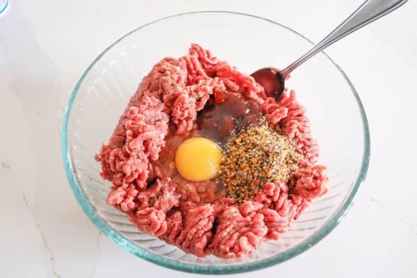 Raw ground hamburger, spices and egg in a large glass bowl.