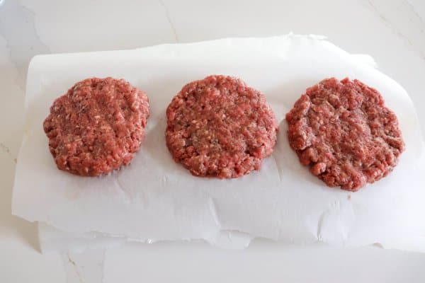 Three raw hamburger patties on a sheet of parchment paper.