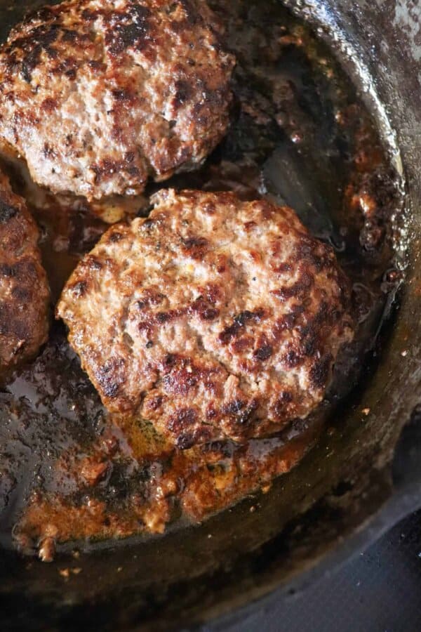 Cast iron skillet with a cooked hamburger patty.