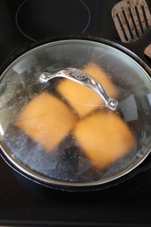 Skillet burgers with a clear lid covering the skillet.