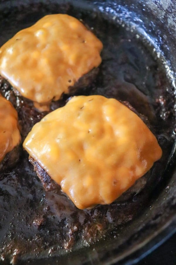 Close up of cooked burger on a cast iron skillet with melted orange cheese on top.