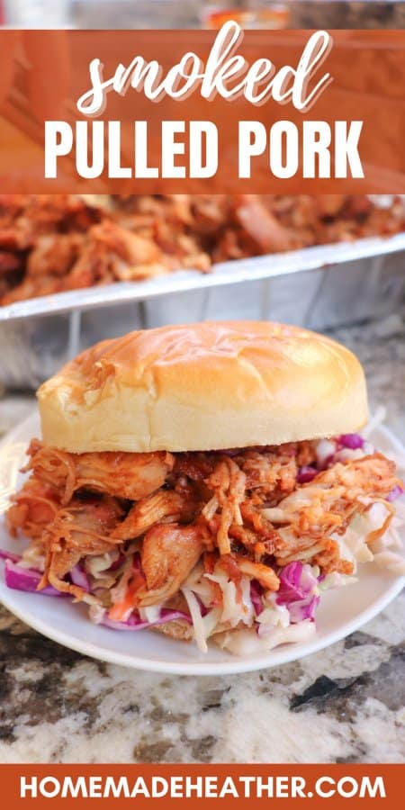 Smoked pulled pork on a white bun with coleslaw on a white plate with a tray of pulled pork in the background.