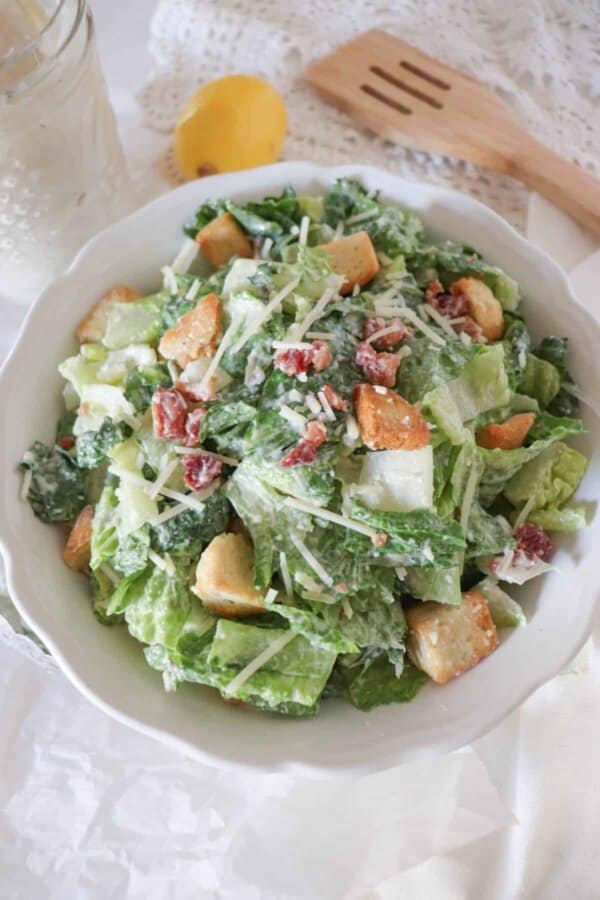 A white bowl with a classic Caesar salad with bacon bits, croutons, and parmesan cheese.