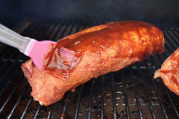 Basting Traeger pulled pork with barbecue sauce with a basting brush.