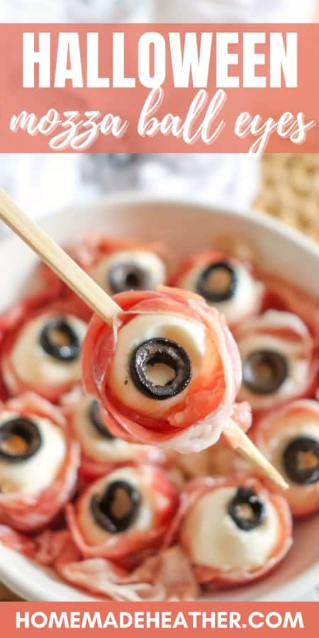 A plate of Halloween mozza eyesโmozzarella balls wrapped in prosciutto, each topped with a black olive slice to resemble an eyeball. One is skewered and held above the plate, highlighting the spooky theme. Text reads Halloween mozza ball eyes.