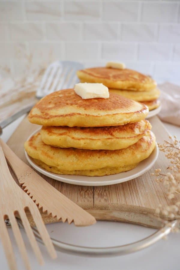 A pat of butter on top of a stack of cornmeal pancakes.