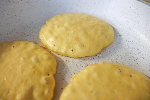 Cornmeal pancakes with bubbles in a frying pan.