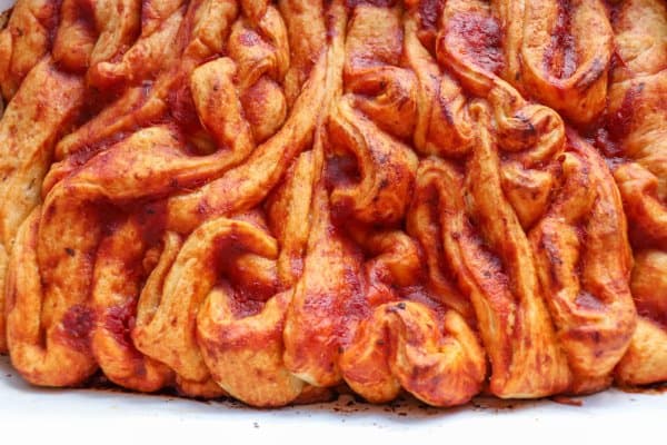 Pizza in the shape of intestines in a white casserole dish.