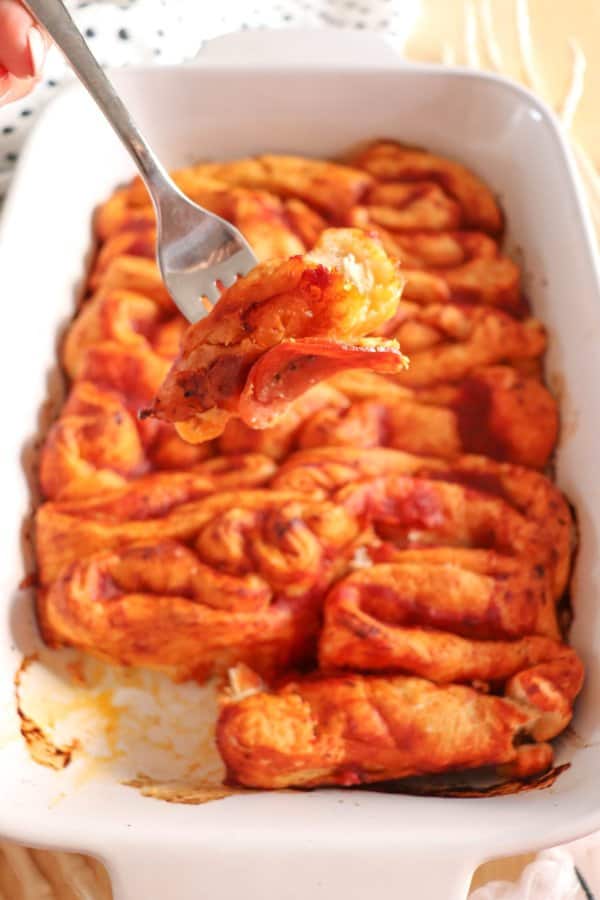 Pizza in the shape of intestines in a white casserole dish with a fork taking a bite.