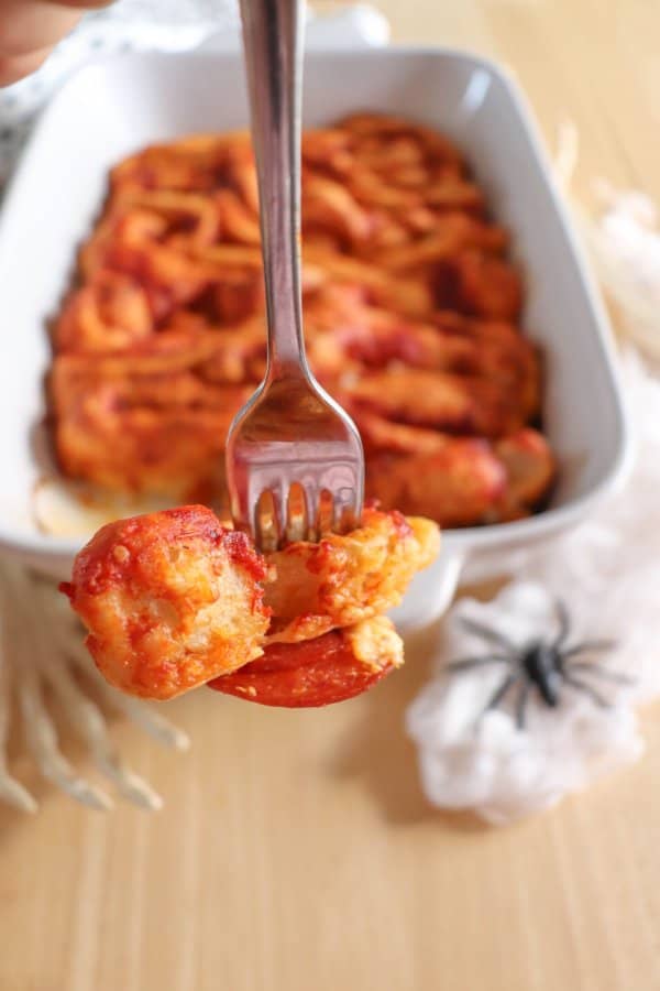 Pizza in the shape of intestines in a white casserole dish with a fork in it.