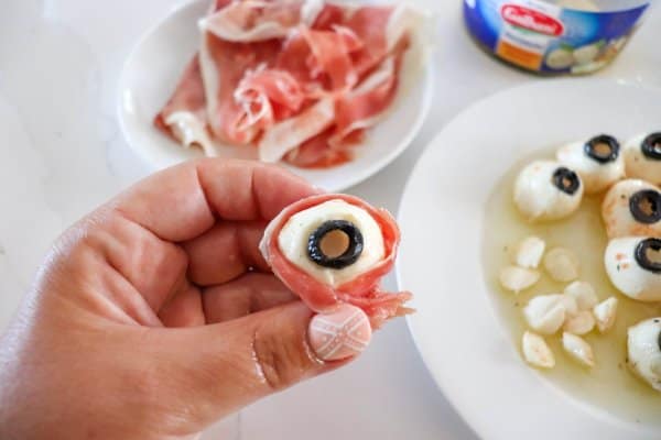 Mozza ball eye wrapped in prosciutto being held in a hand.