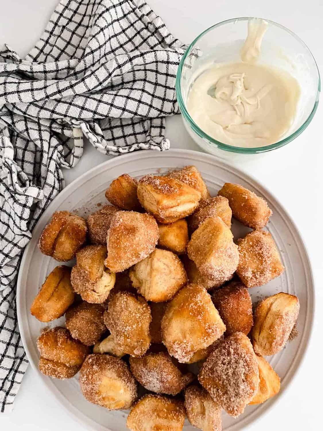 Air fryer donut holes on a plate with icing in a glass bowl beside.