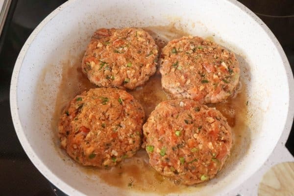 Four raw salmon burgers in a white skillet.