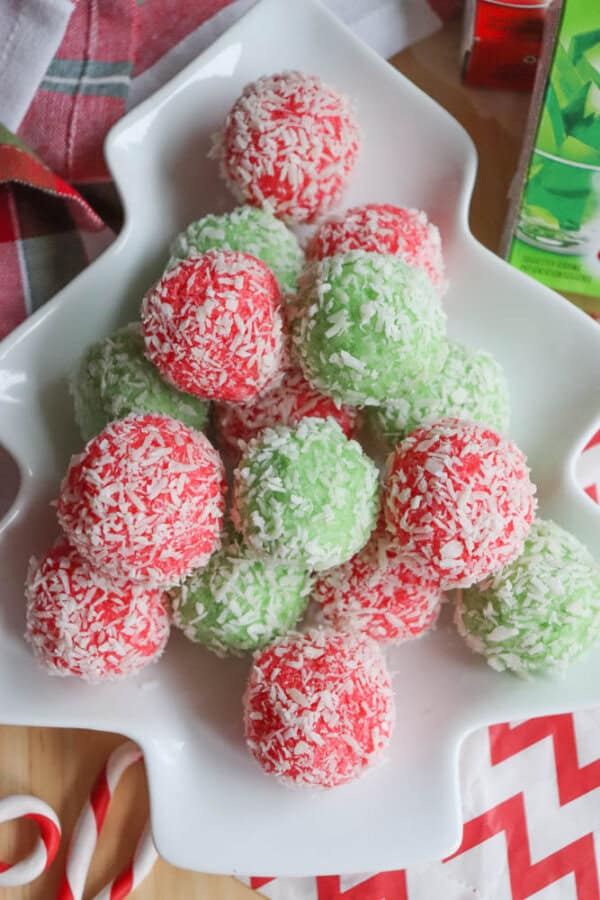 A decorative tree-shaped plate holds red and green coconut-covered truffles. Reminiscent of a festive thin mint cookie recipe, the truffles are piled in alternating colors, with holiday-themed decor visible in the background.