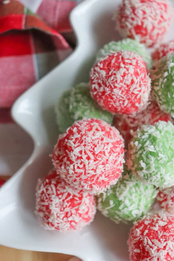 A white dish filled with red and green coconut-covered balls, resembling festive treats, sits on a checkered red and white napkin in the background, evoking the charm of a thin mint cookie recipe.