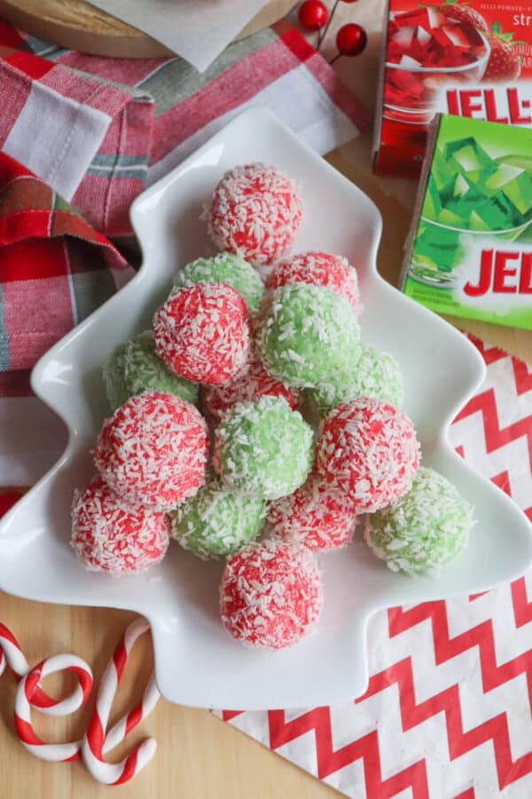 A festive dish features coconut-covered balls with hints of strawberry and lime on a Christmas tree-shaped plate. The scene, decorated with candy canes, is set against a red and white checkered cloth reminiscent of holiday gatherings. Nearby, a thin mint cookie recipe adds extra seasonal delight.