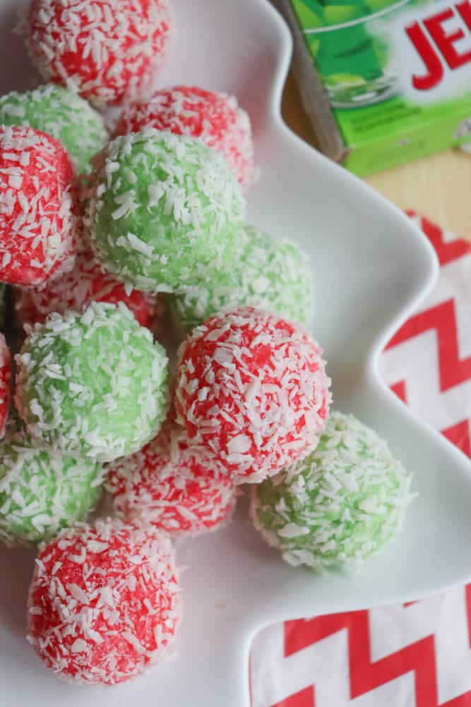 A white dish holds a pile of red and green coconut-covered dessert balls, reminiscent of holiday treats. In the background, a red and white zigzag-patterned fabric complements a box of green Jell-O, almost like ingredients waiting for a thin mint cookie recipe adventure.