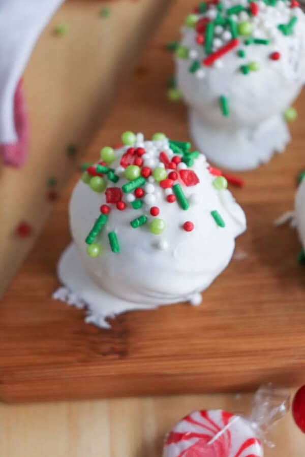 A festive rocky road treat covered in white icing and topped with red, green, and white sprinkles sits on a wooden board. A peppermint candy lies nearby, complementing the holiday-themed presentation with an irresistible charm reminiscent of crockpot candy delights.