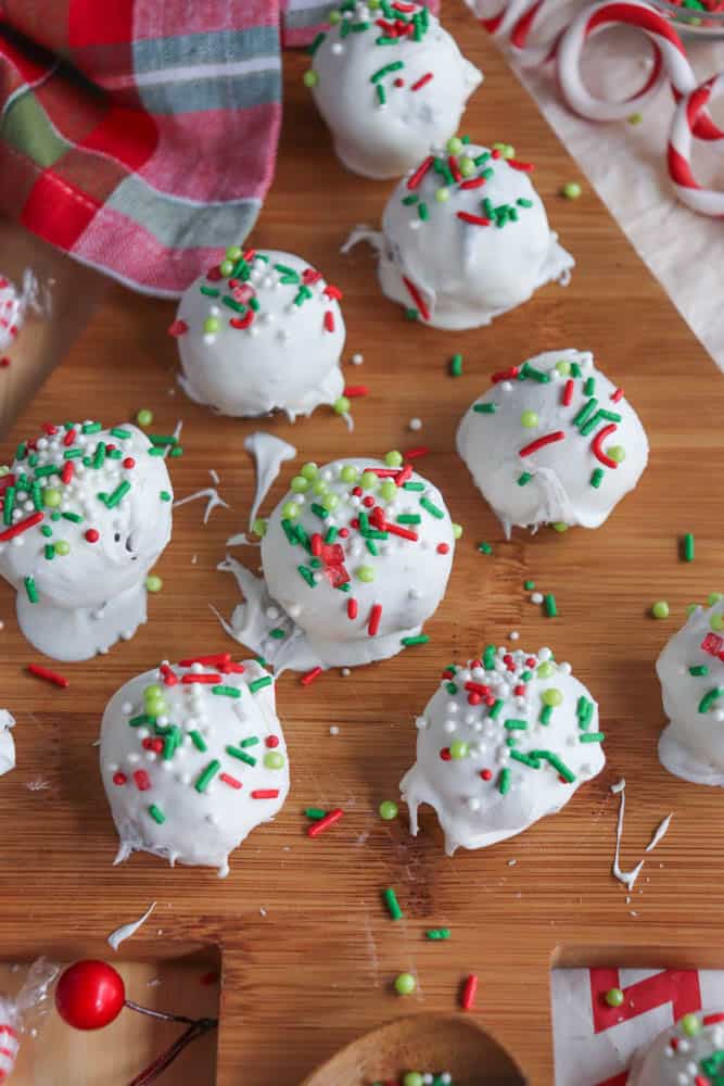 White chocolate truffles coated with festive red, green, and white sprinkles are arranged on a wooden board. A red and green plaid cloth and some candy canes set the holiday scene, reminiscent of rocky road crockpot candy delights.