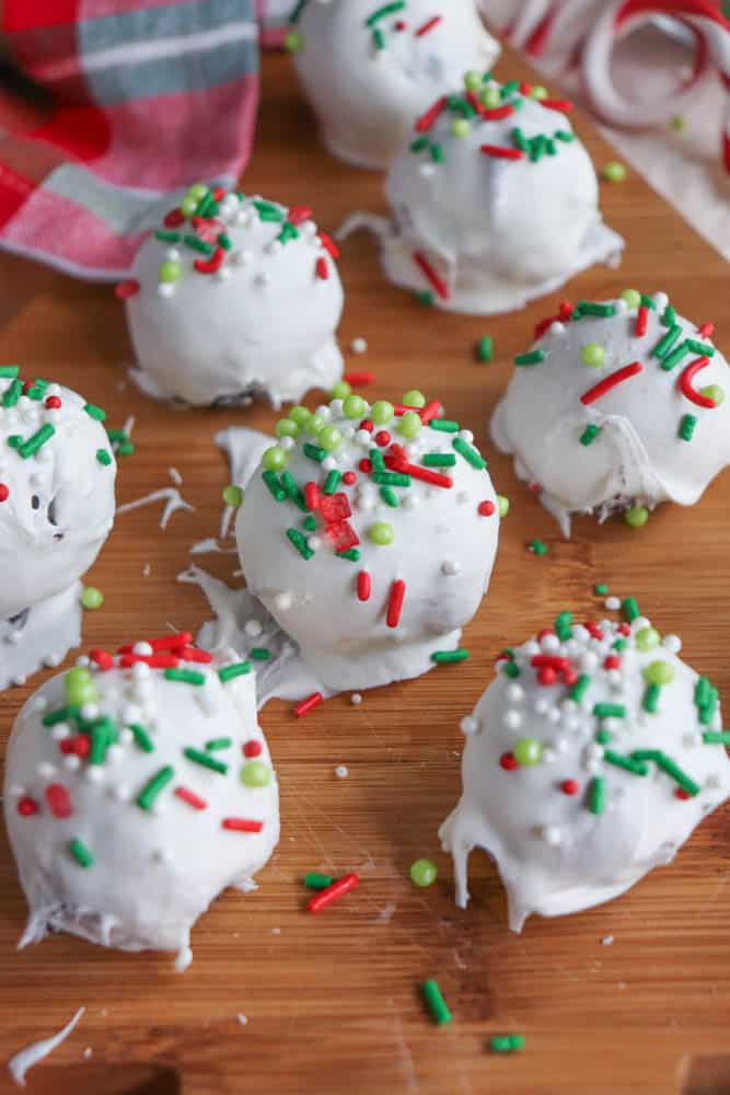 White chocolate truffles adorned with red, green, and white sprinkles are elegantly arranged on a wooden surface. A hint of a red and green checkered cloth peeks from the background, adding a festive touch reminiscent of rocky road crockpot candy creations.