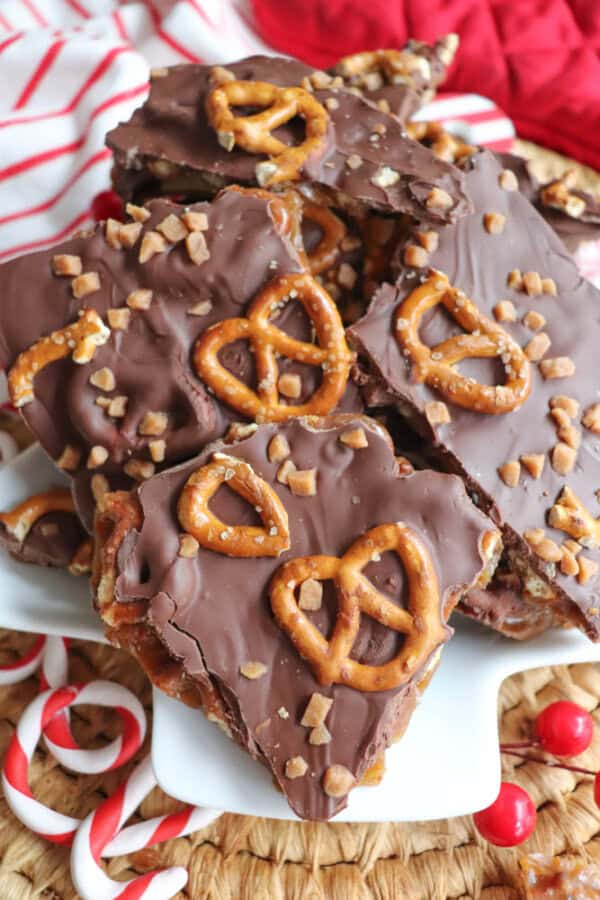 Christmas Cracker Toffee A plate of rocky road chocolate bark topped with pretzels and toffee bits. The bark is arranged in a pile, set against a background of red and white striped fabric and scattered peppermint candies, creating a festive mood akin to the simplicity of crockpot candy.