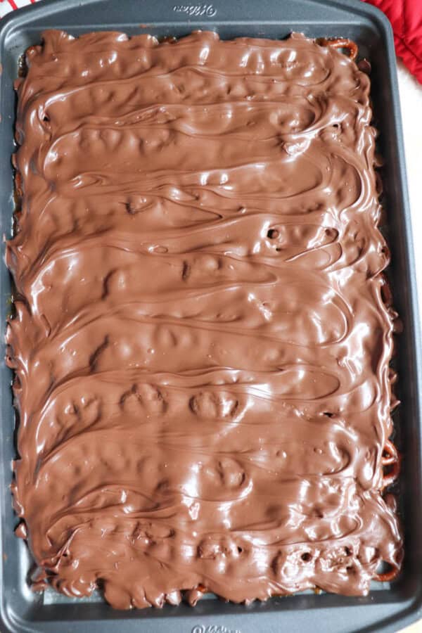 A baking tray filled with a chocolate-covered dessert, reminiscent of rocky road candy, featuring a smooth and glossy surface with rippled textures.