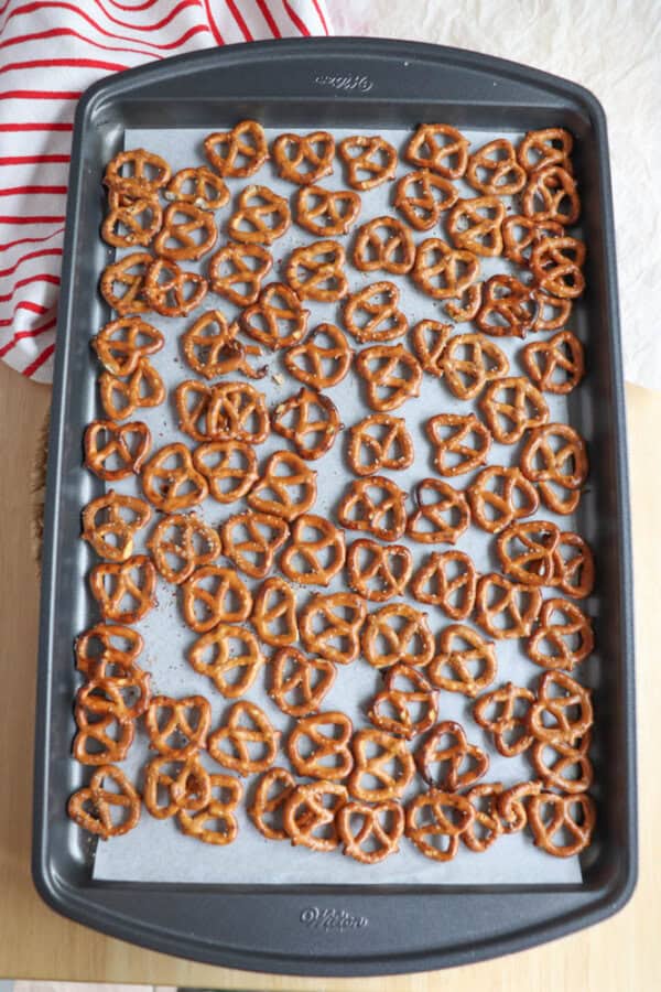 A baking tray filled with evenly spread small pretzels rests on parchment paper, ready for their next transformation. A red and white striped cloth is partially visible in the top left corner, adding a touch of charm reminiscent of homemade rocky road crockpot candy creations.