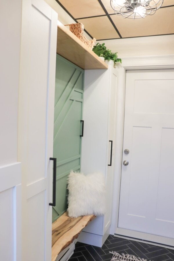 Mudroom with white cupboards, black tile floor, wood ceiling and green feature wall.