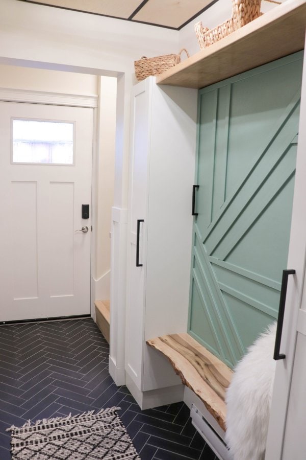 Mudroom with white cupboards, black tile floor, wood ceiling and green feature wall.