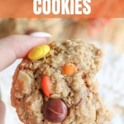 Oatmeal cookies with chocolate chips, orange and yellow M&Ms stacked on a cream plate.