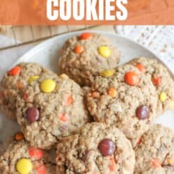 Oatmeal cookies with chocolate chips, orange and yellow M&Ms stacked on a cream plate.