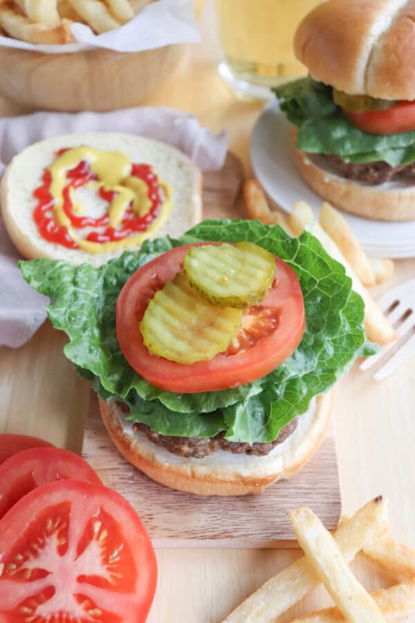 A burger cooked in the air fryer on a bun with lettuce, tomato, and pickles.