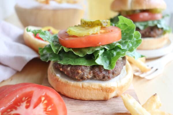 A burger cooked in the air fryer on a bun with lettuce, tomato, and pickles.