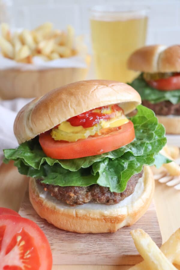 A burger cooked in the air fryer on a bun with lettuce, tomato, pickles,  and condiments.