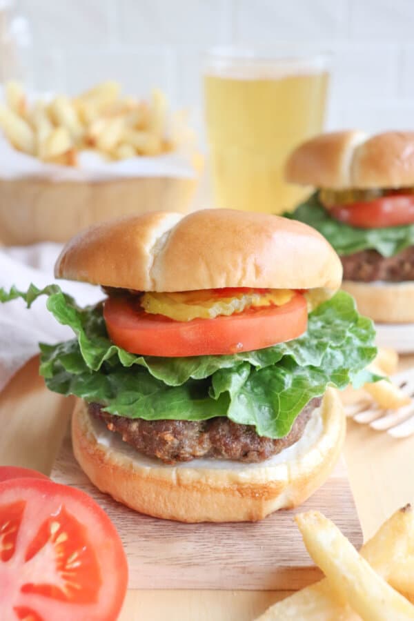 A burger cooked in the air fryer on a bun with lettuce, tomato, and pickles.