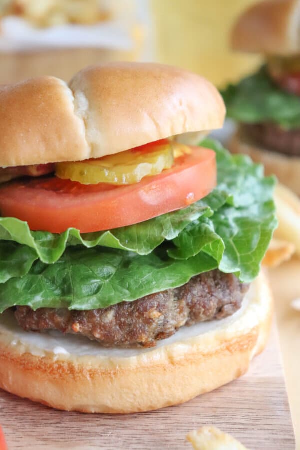 A burger cooked in the air fryer on a bun with lettuce, tomato, and pickles.