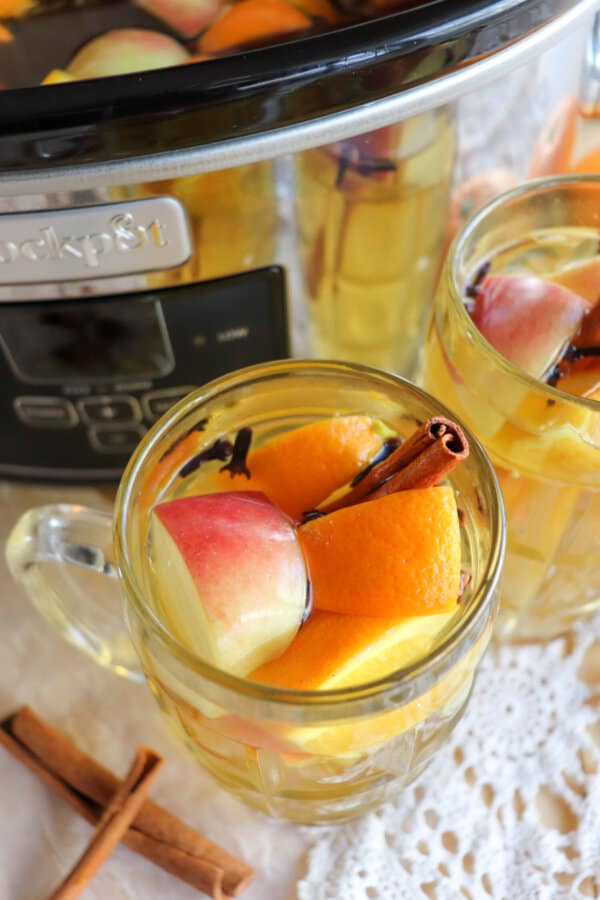 Apple cider in a clear glass with orange and apple slices for garnish.