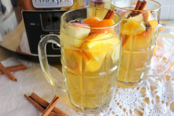 Apple cider in two clear glasses full that have orange and apple slices for garnish.