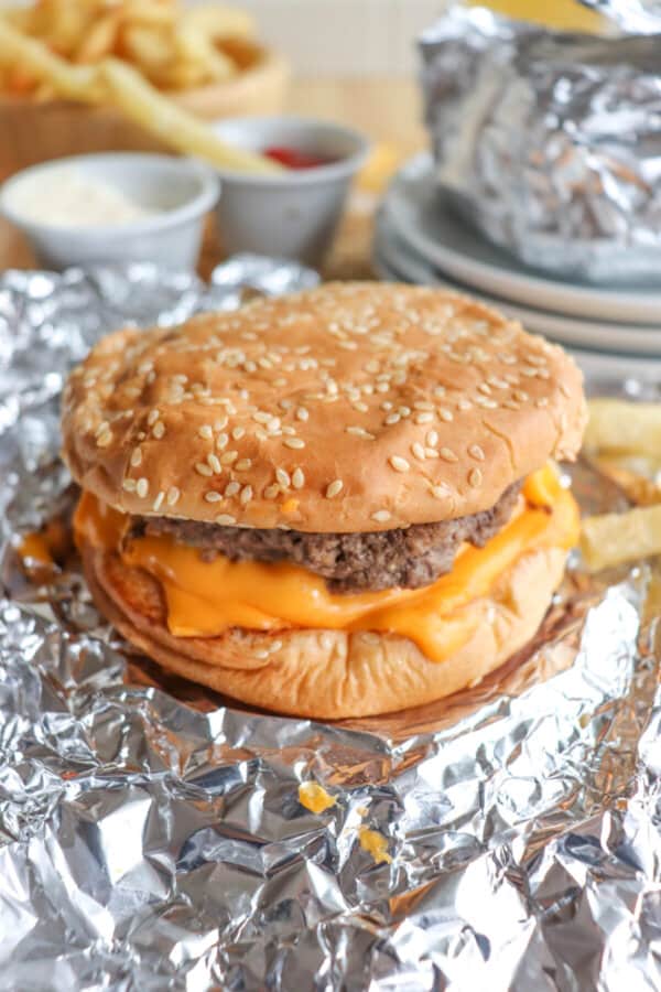 Copycat five guys burger with melted American cheese on a sesame seed bun on foil.